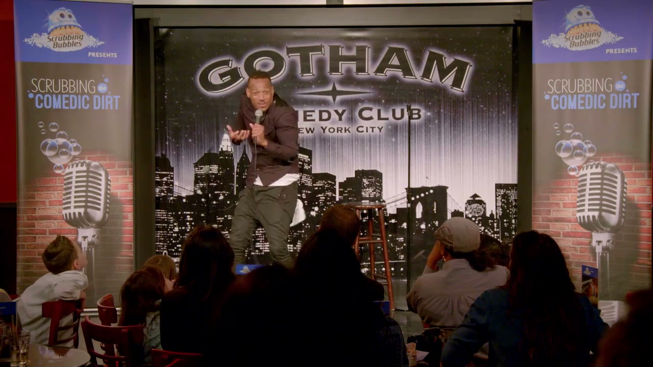 Marlon Wayans performs on a stage branded Scrubbing the Comedic Dirt.