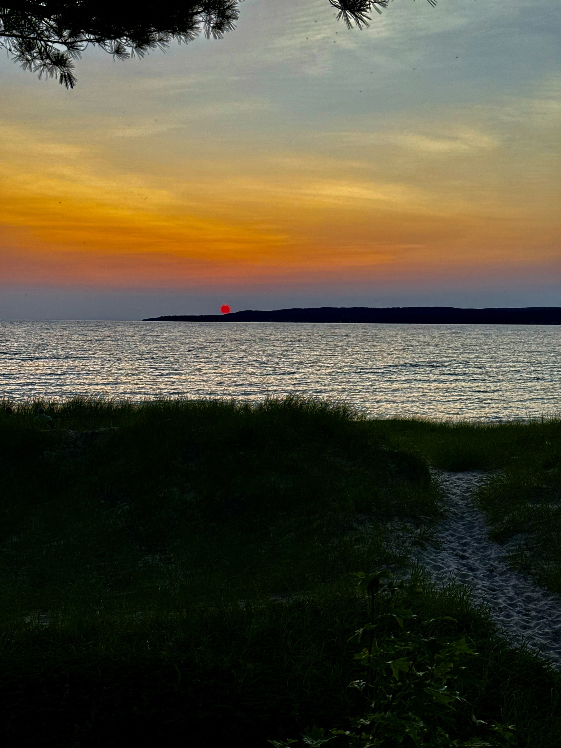 A red-orange sunset over a lake, photographed from a wooded shoreline.
