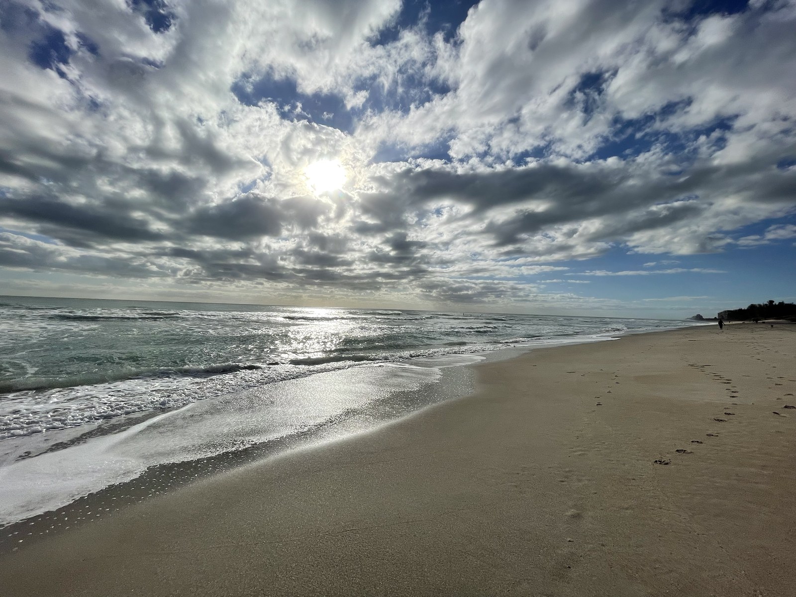 Sunlight breaking through dramatic clouds above a wide beach and ocean horizon.